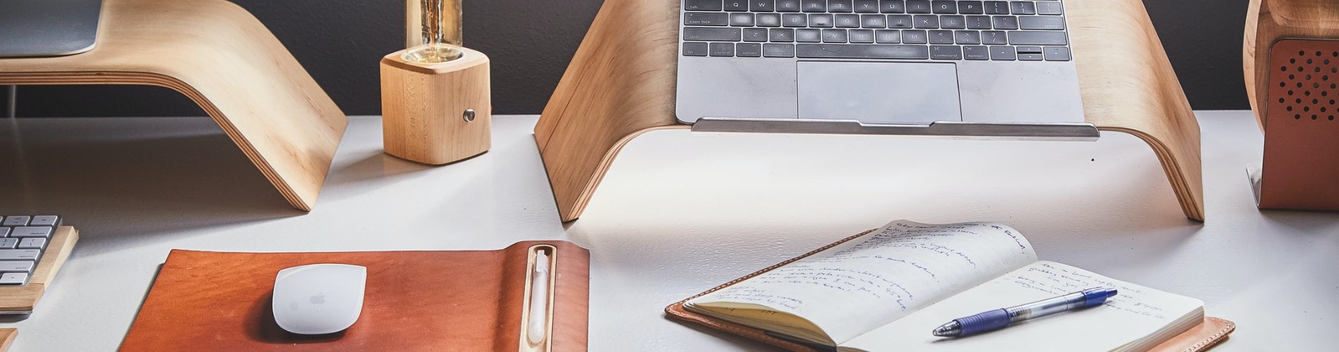 A computer mouse, notepad and pen below a laptop on a desk