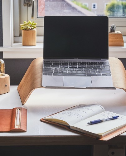 A laptop on a stand with a notebook and pen below it
