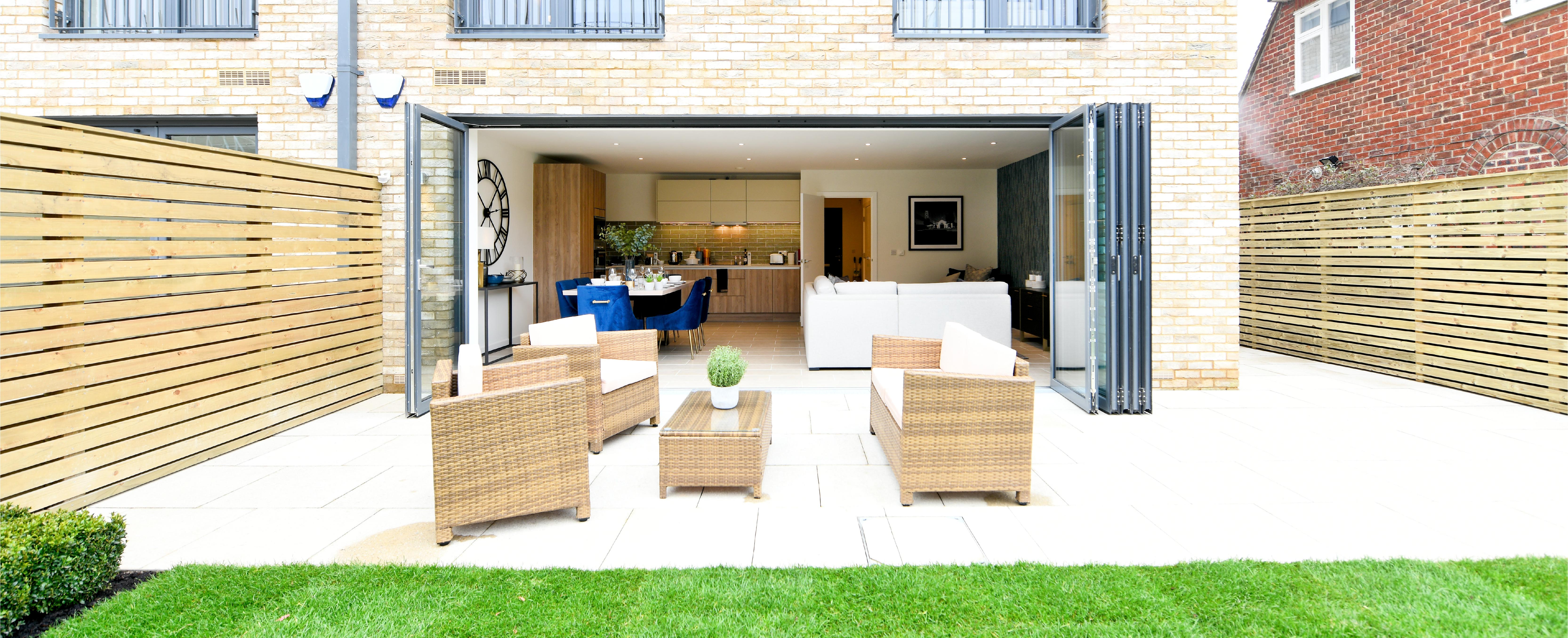 Garden area with stylish wicker furniture and doors folded open fully to reveal kitchen space
